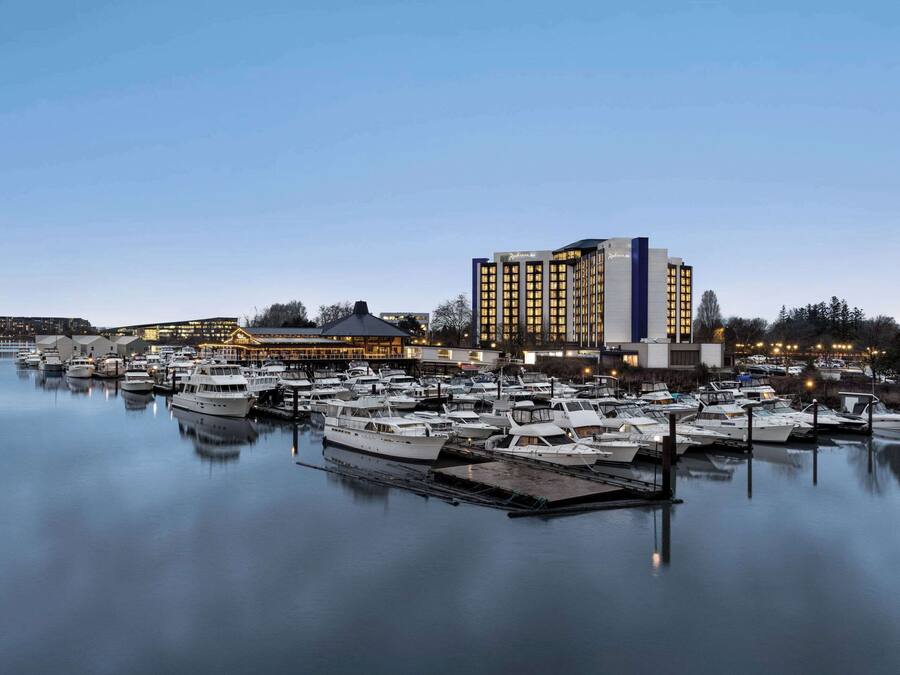 Marina com vários barcos atracados, um grande edifício de hotel e uma área costeira bem iluminada.