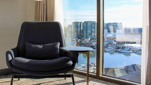 Una habitación moderna con un ventanal grande, un sillón negro, una mesita redonda y una lámpara.