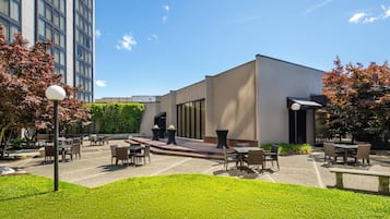 An outdoor patio area with tables and chairs, a modern building with large windows, and a clear blue sky.