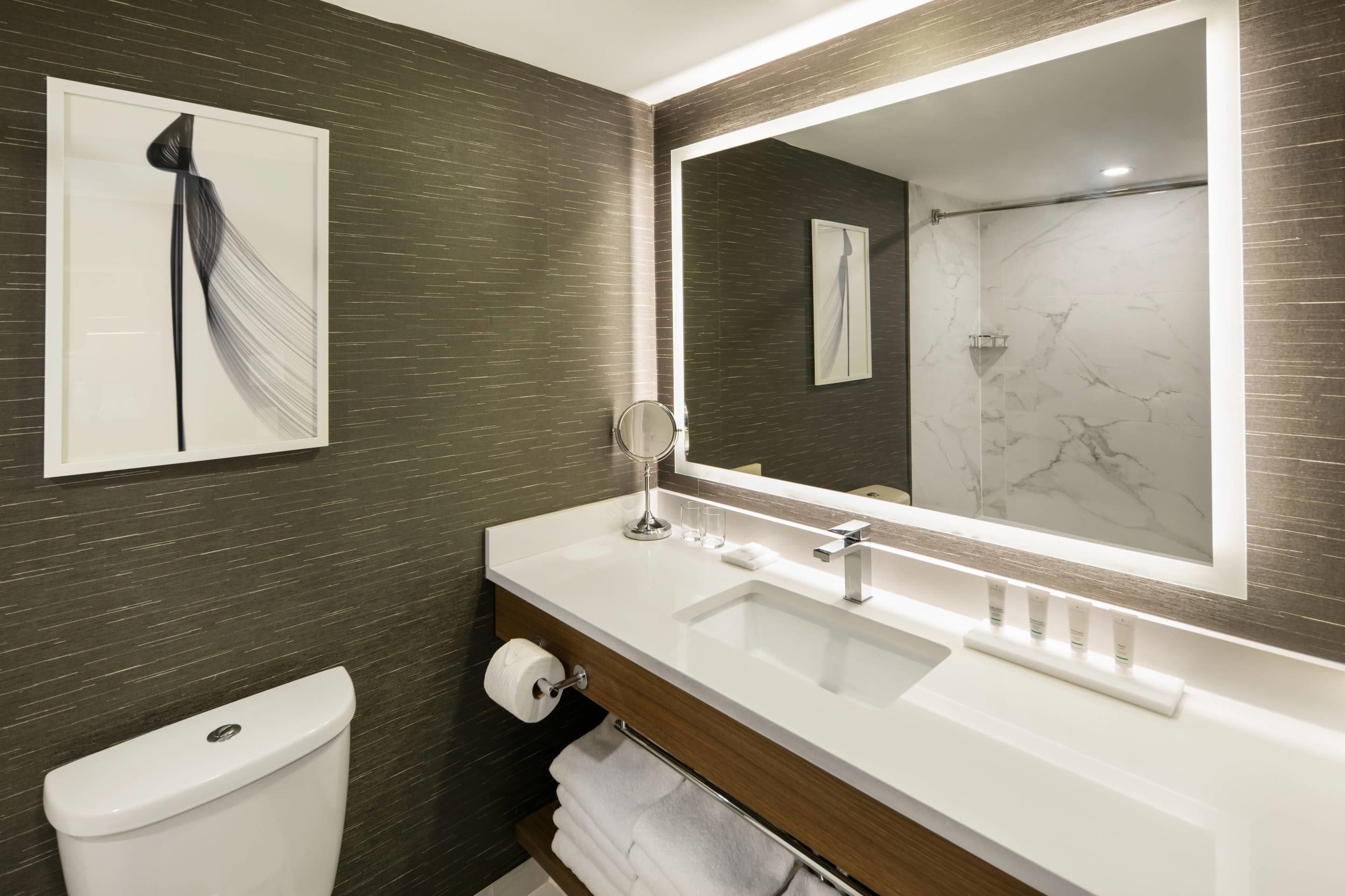 Une salle de bain moderne avec un grand miroir, des toilettes et un meuble-lavabo doté d’un évier et d’un porte-serviettes.