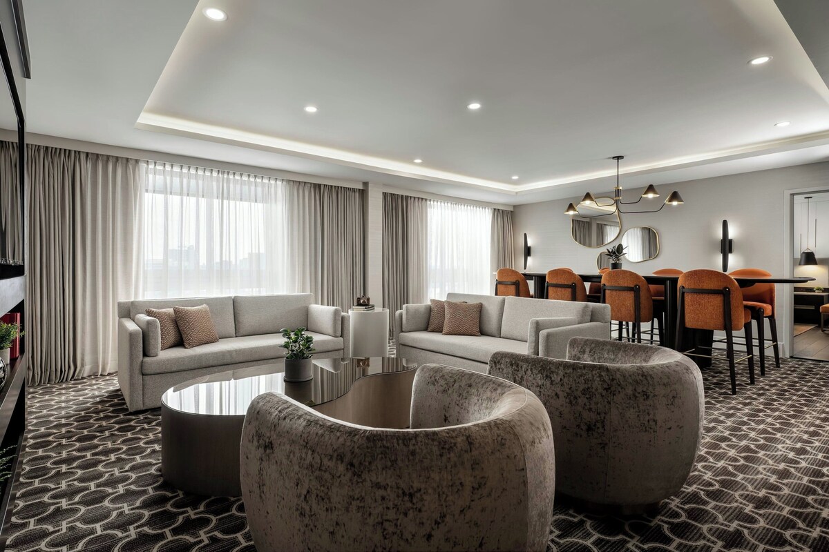 Una moderna camera d'hotel con angolo living, divanetto, tavolino e zona pranzo con sedie e tavolo.