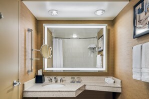 A bathroom with a large mirror, a sink, a shower, and a towel rack.