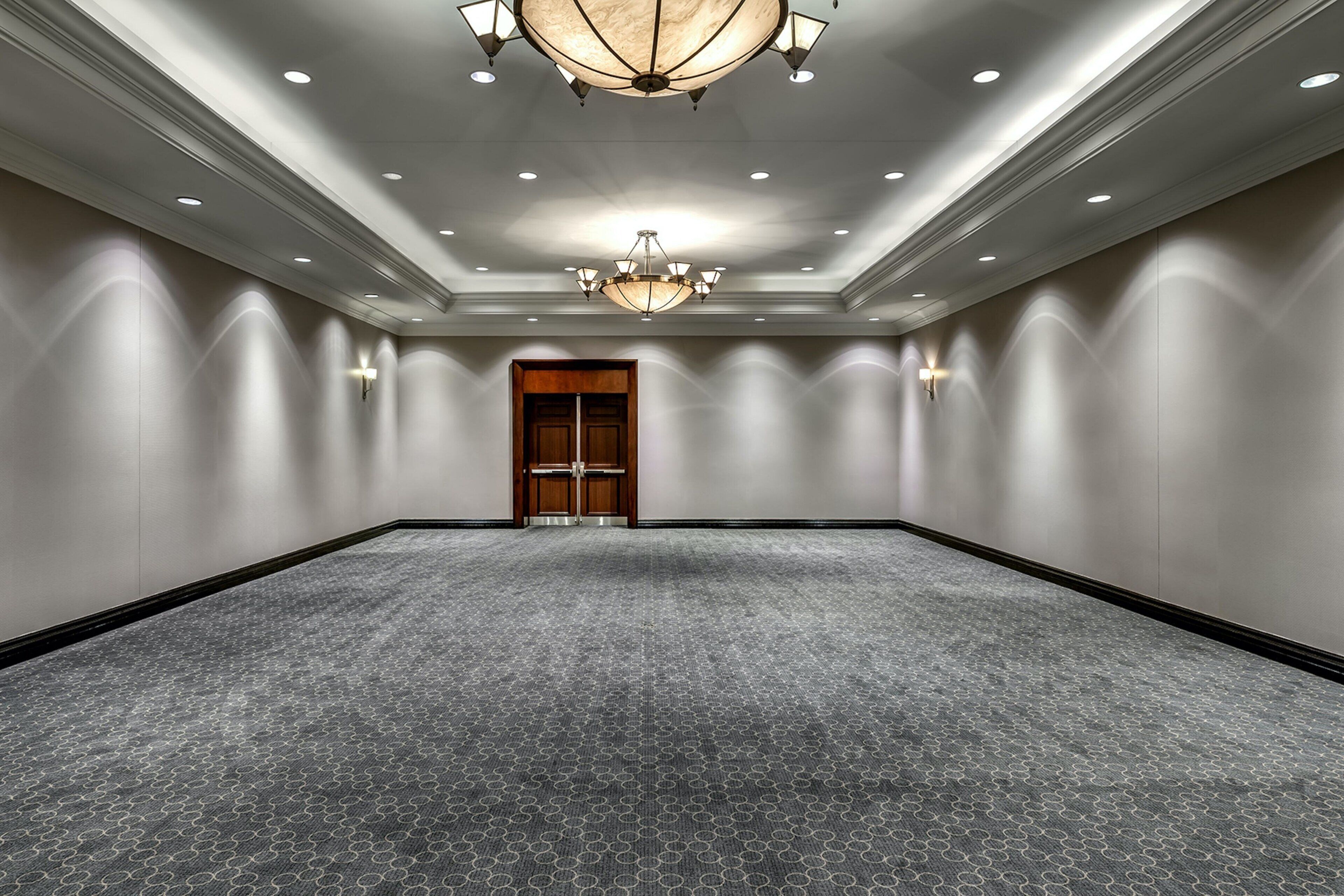 A large, empty conference room with a patterned carpet, recessed lighting, and a chandelier.