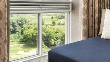A bedroom with a large window offering a view of a green landscape.