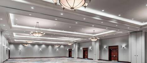 A spacious conference room with a patterned carpet, multiple chandeliers, and recessed lighting.