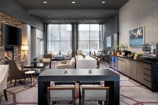 Un moderno vestíbulo de hotel con una amplia zona de estar, una cocina y grandes ventanales con vistas a la ciudad.