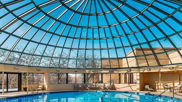 A swimming pool with a glass dome ceiling, lounge chairs, and a view of trees outside. - Sheraton Toronto Airport Hotel & Conference Centre (Toronto)
