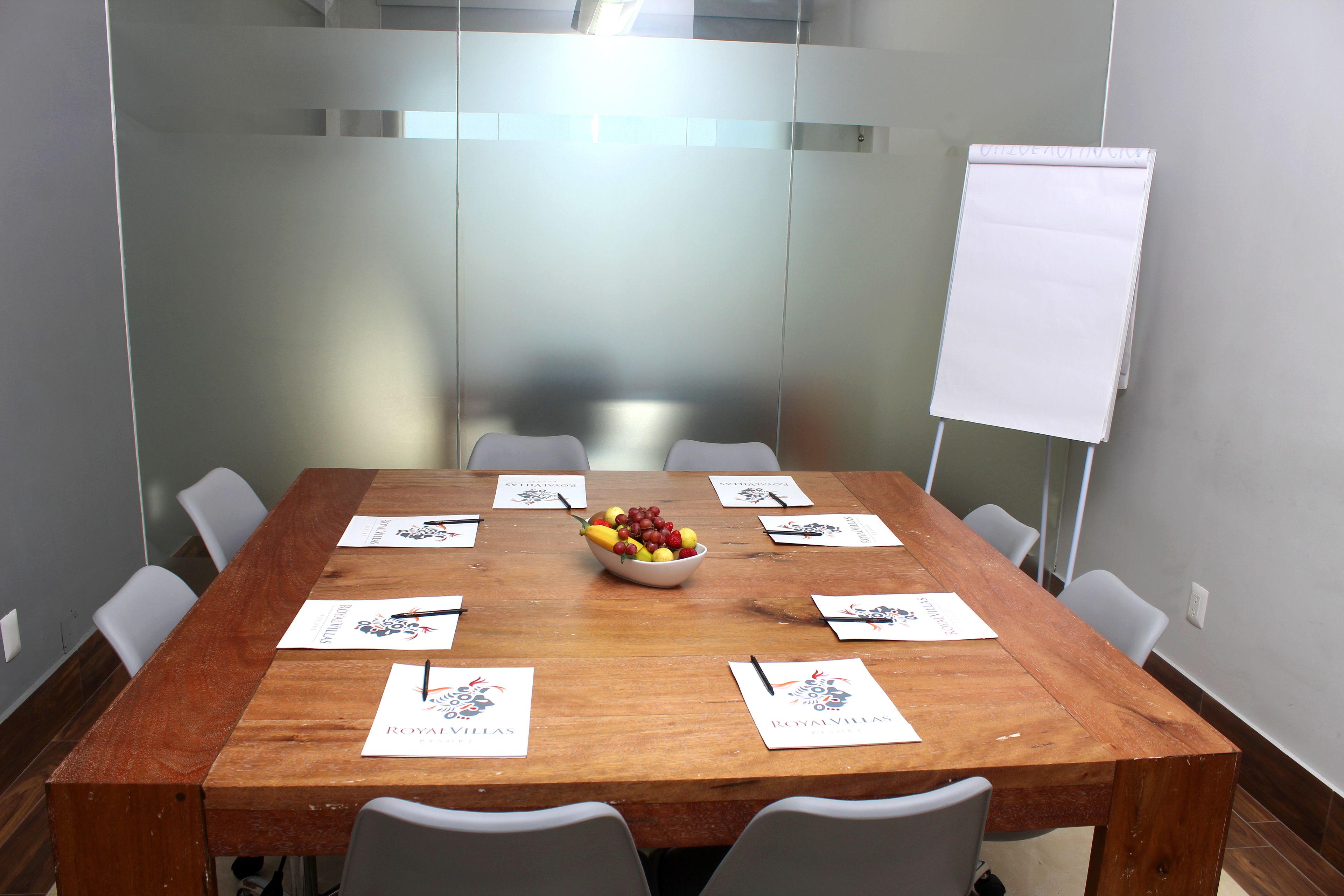 A conference room with a wooden table, white chairs, a whiteboard, and a bowl of fruit.