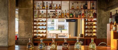 Una zona de bar con una variedad de botellas de licores exhibidas en estanterías y una selección en la barra.