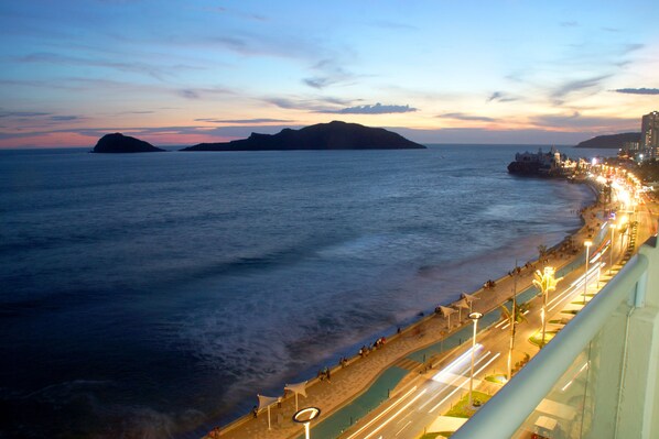 A coastal cityscape with a promenade along the waterfront, featuring a clear view of the sea and distant islands.