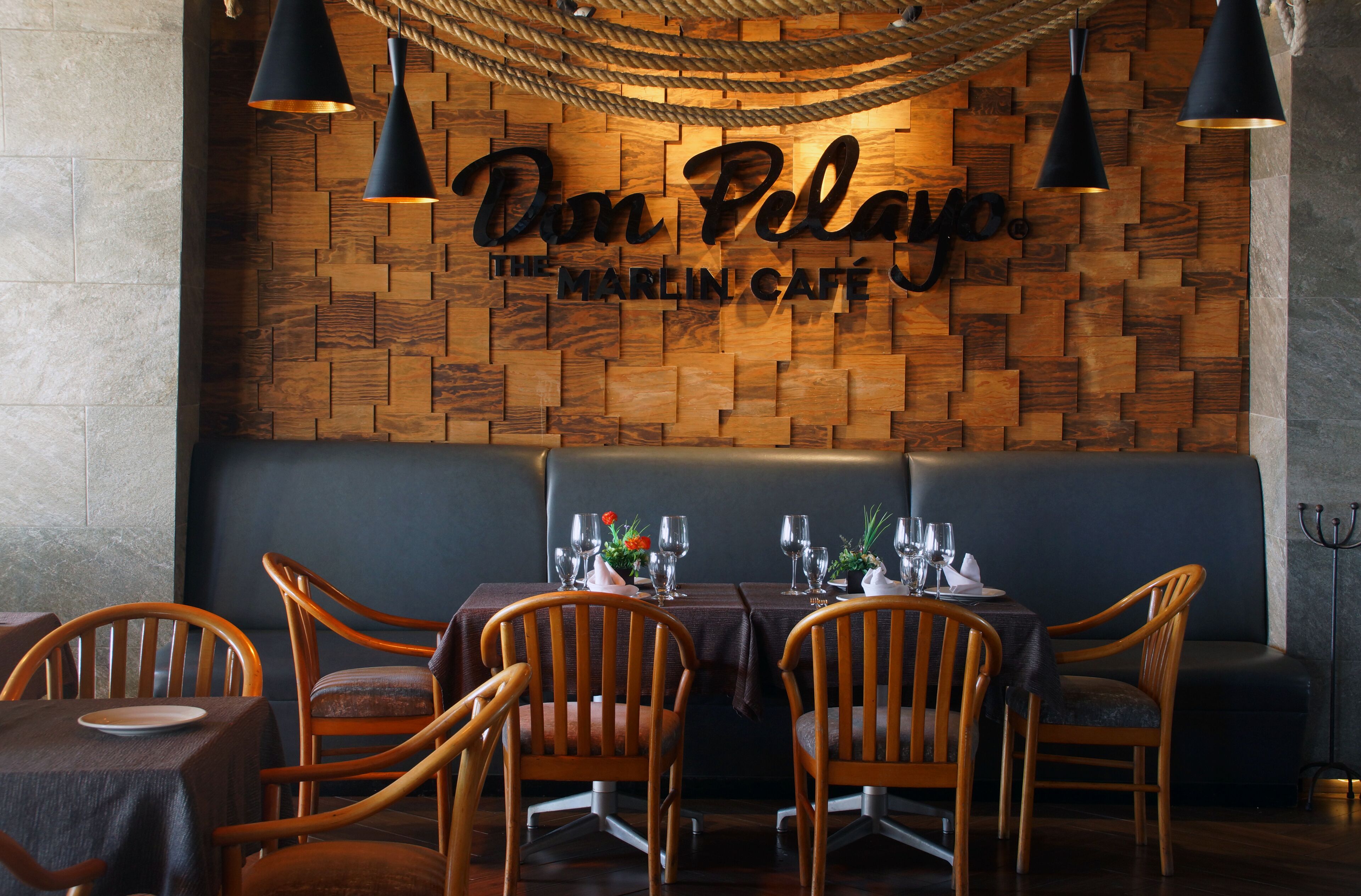 A cozy restaurant interior with wooden wall decor, a dark seating area, and tables set for dining.