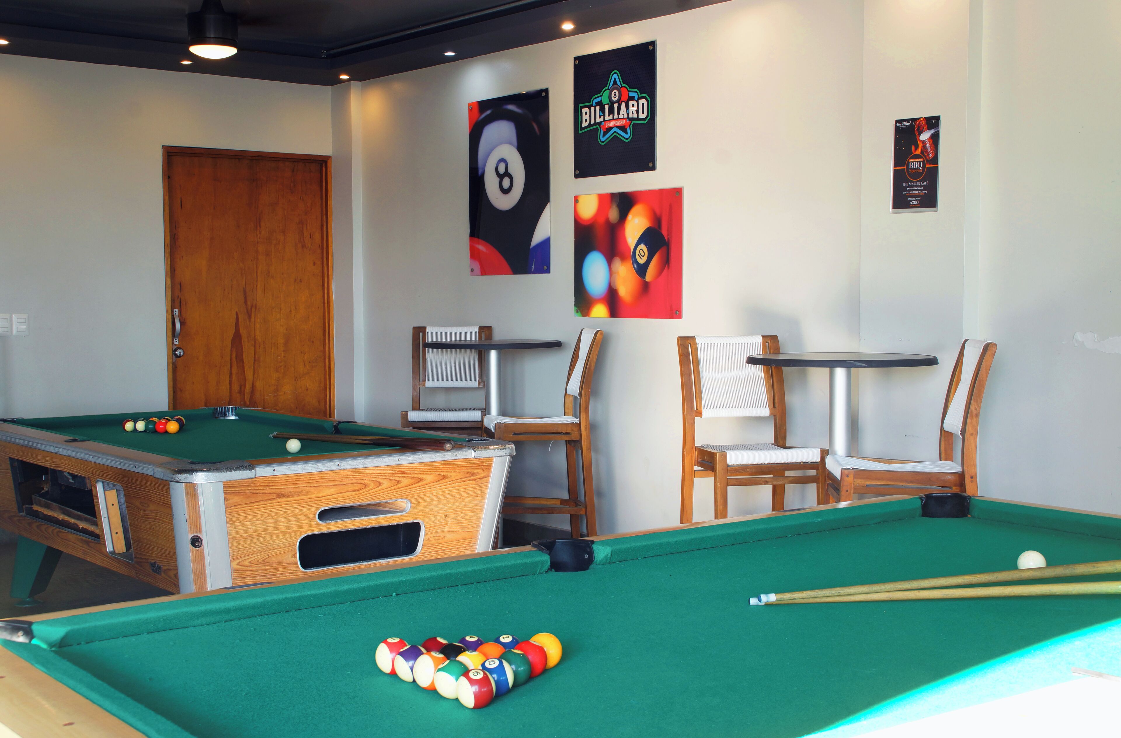 A pool table with balls, a wooden door, and two chairs.
