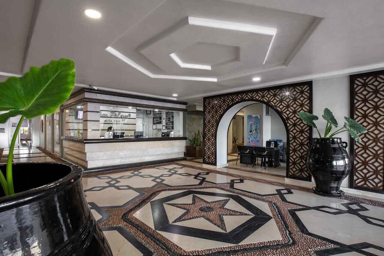 A hotel lobby with a reception desk, a patterned floor, and a decorative wall.