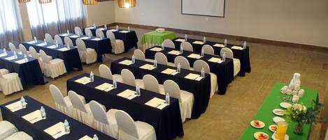 A conference room with rows of tables, chairs, and a buffet table with food and drinks.