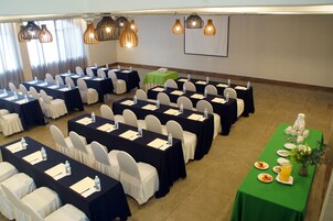Un salón de conferencias con filas de mesas, sillas y una mesa de buffet con comida y bebidas.