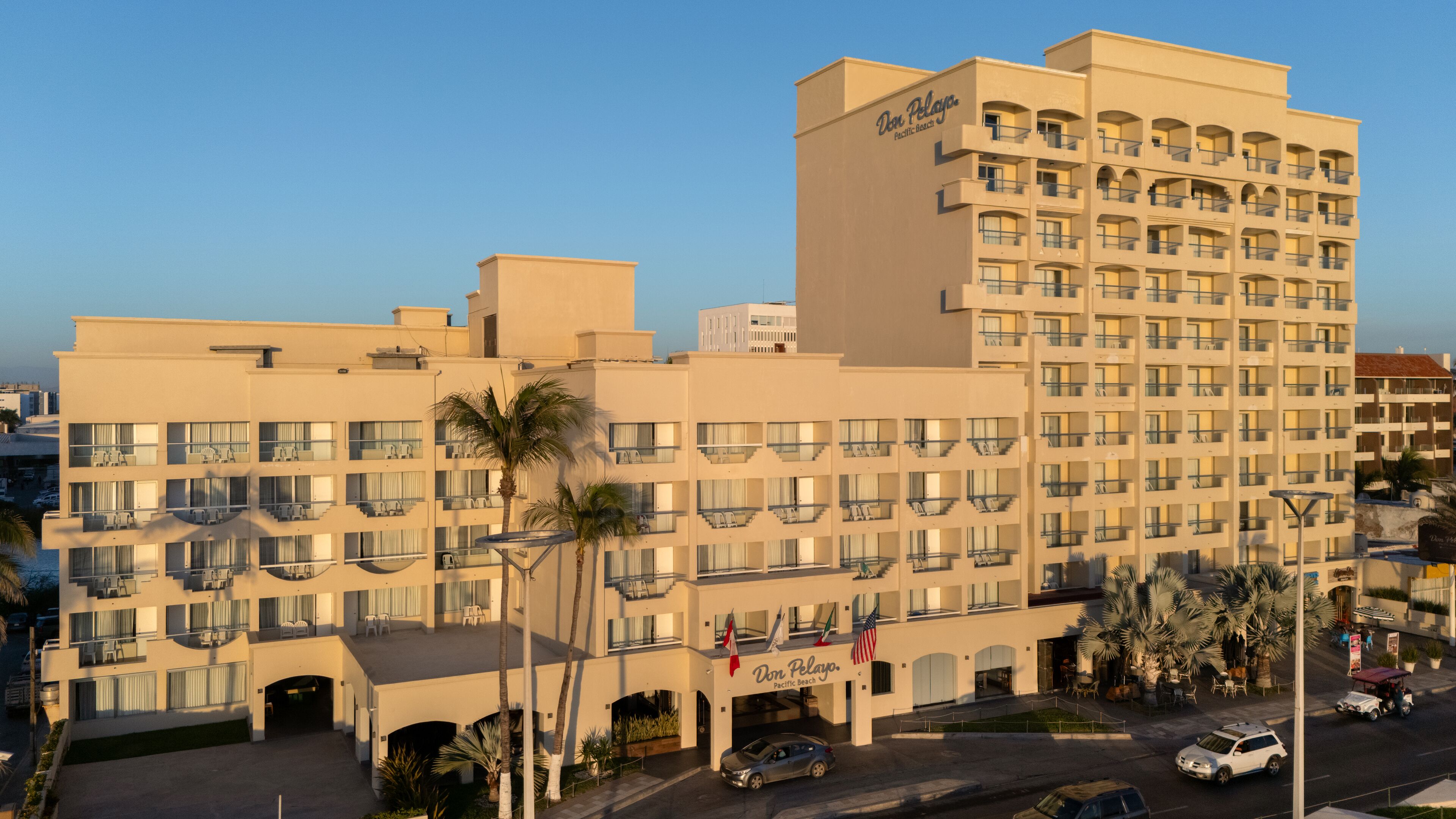 A multi-story hotel with balconies, a central courtyard, and palm trees.