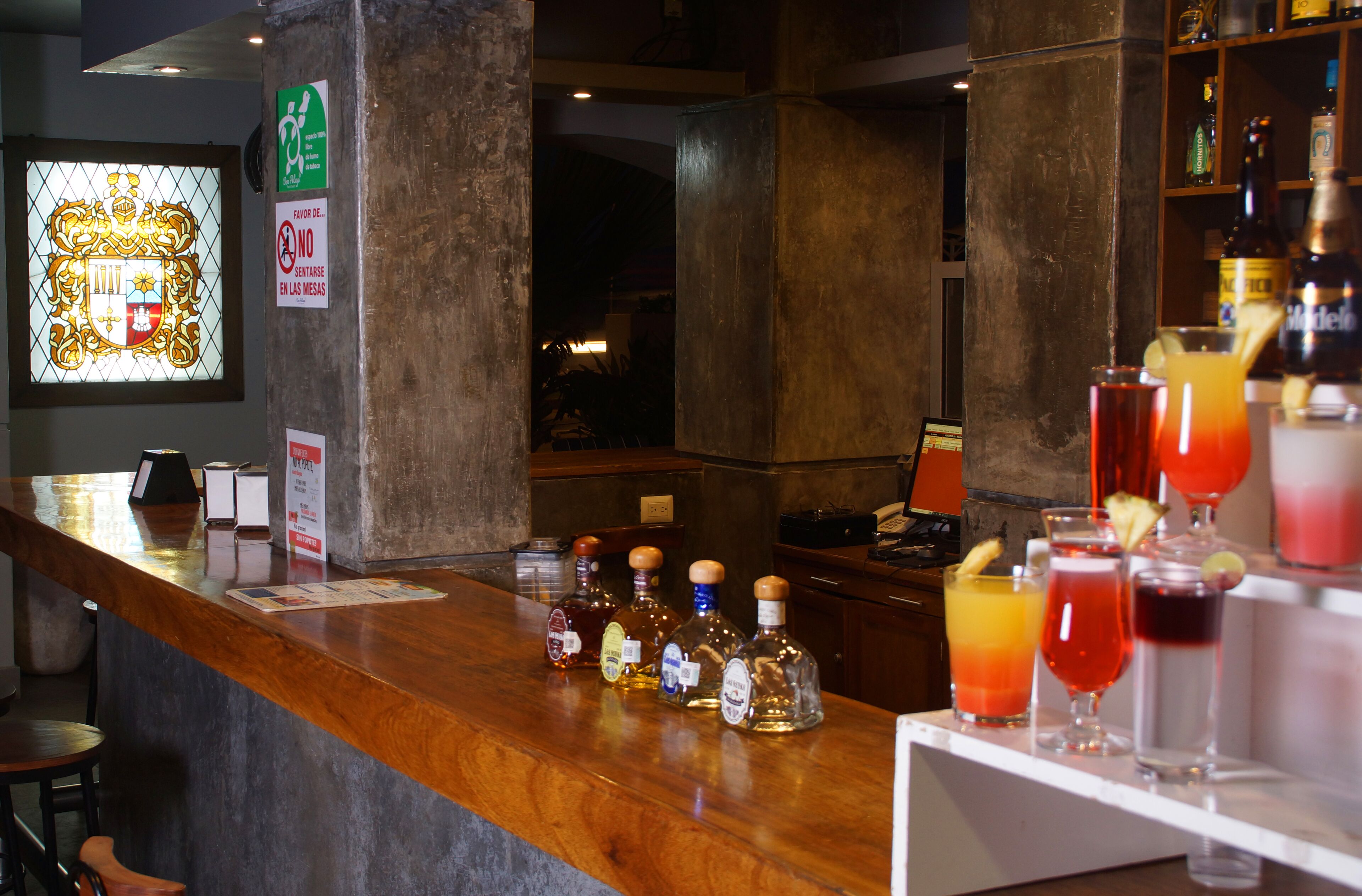 A bar area with a wooden counter, bottles of liquor, and various drinks.