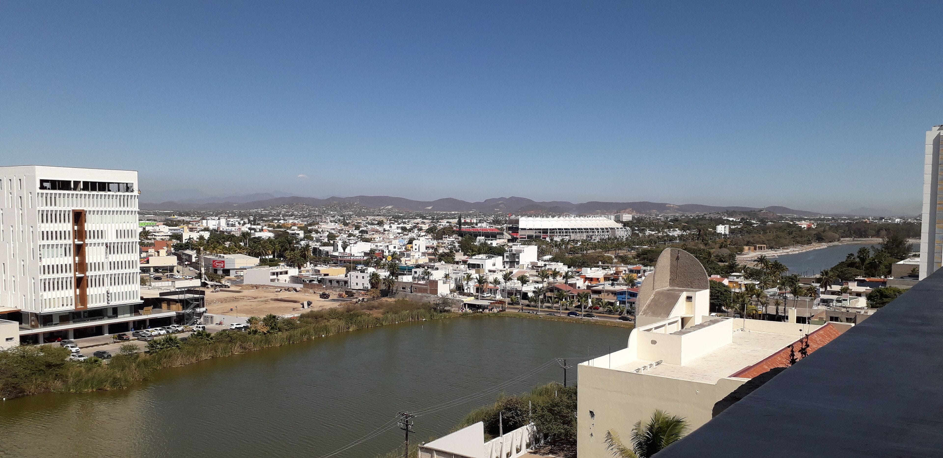A cityscape with a river, buildings, and mountains in the distance.