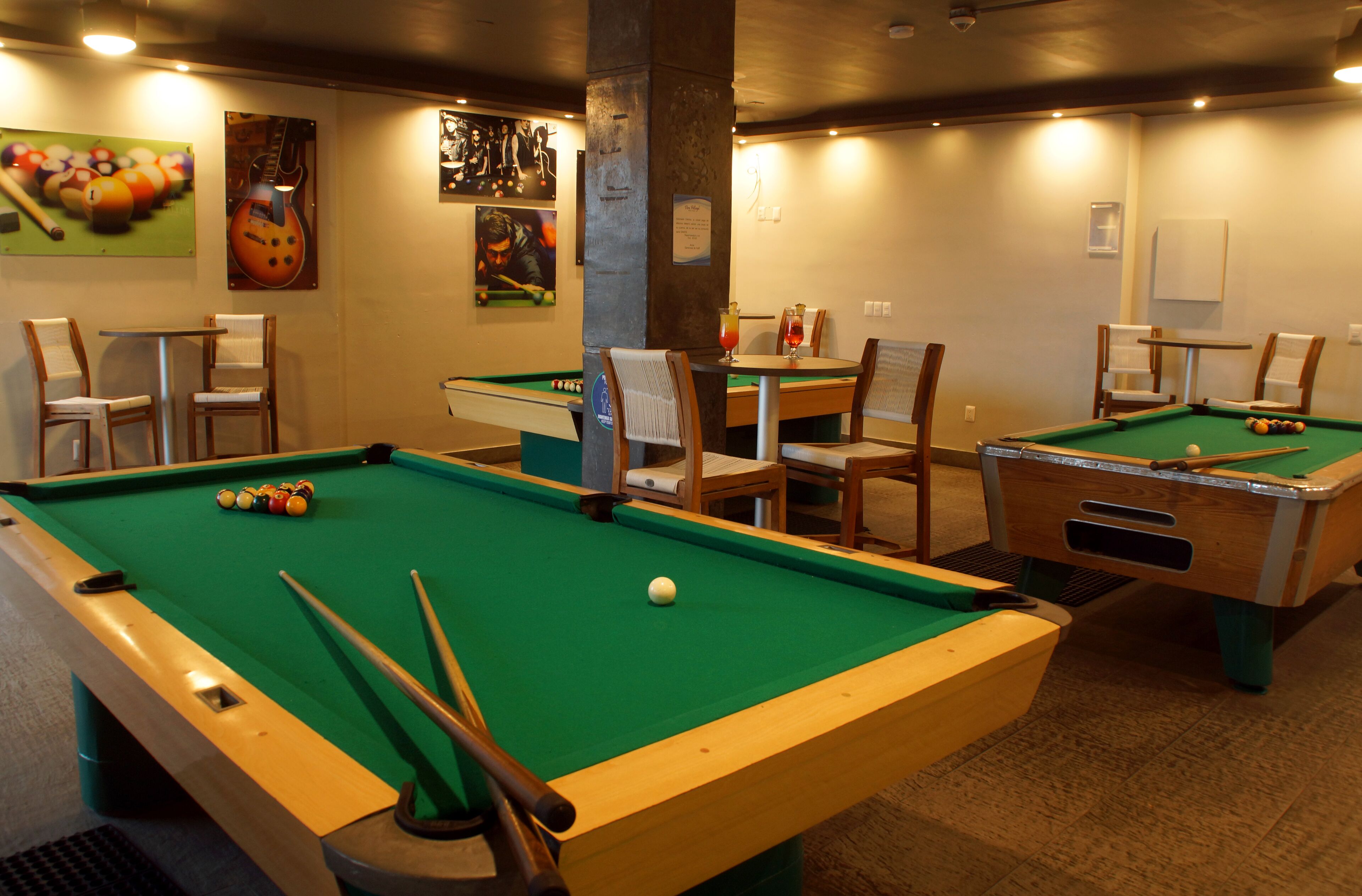Une table de billard recouverte d’un drap vert, entourée de chaises en bois et d’une table.