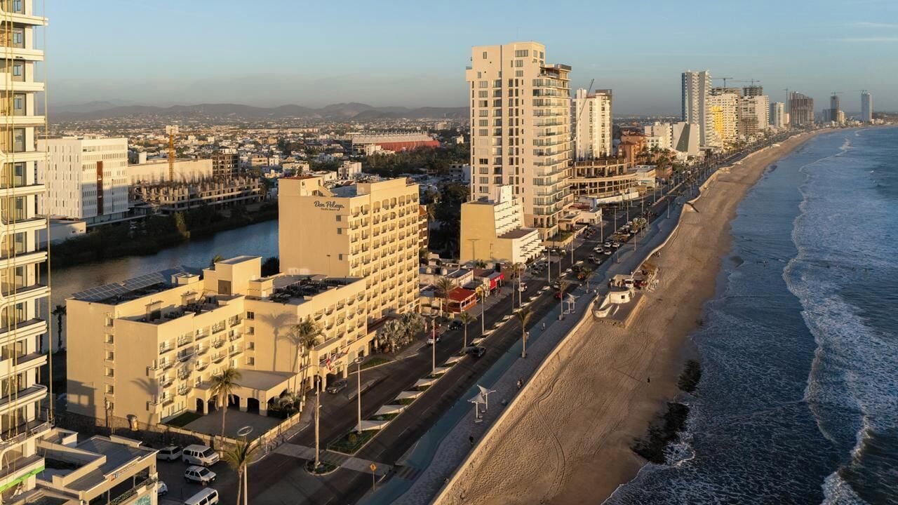 A coastal cityscape with high-rise buildings, a beach, and a river.