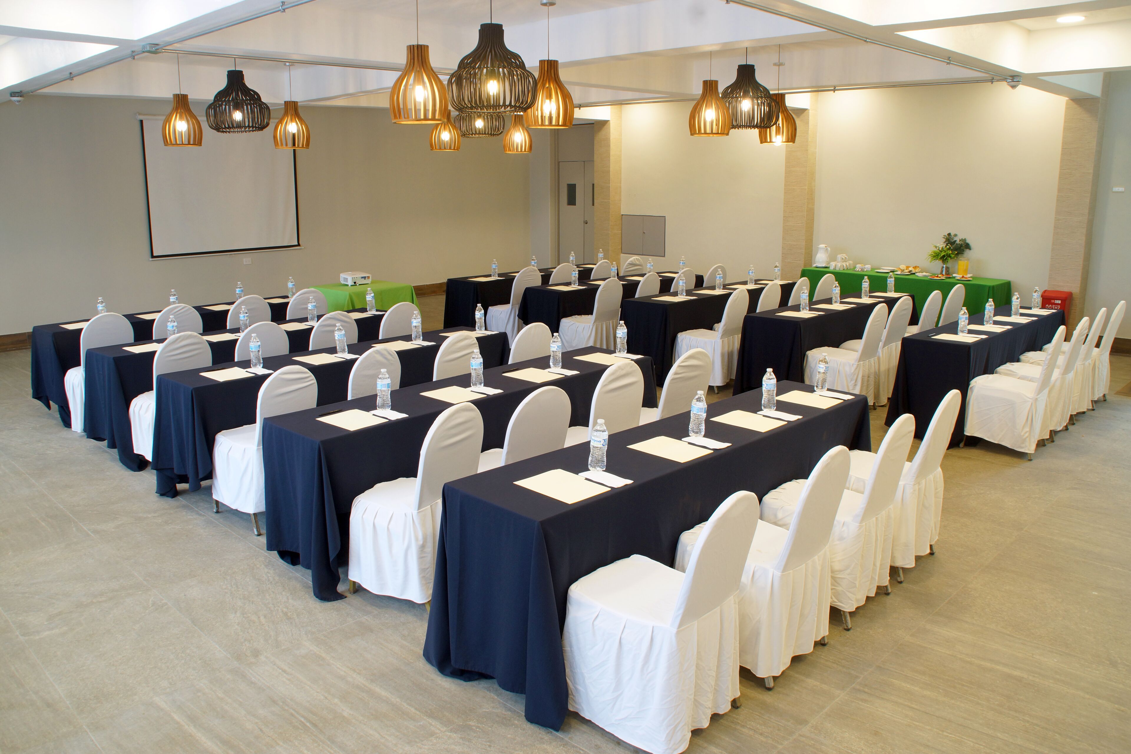 A conference room with multiple tables, white chairs, and overhead lighting.