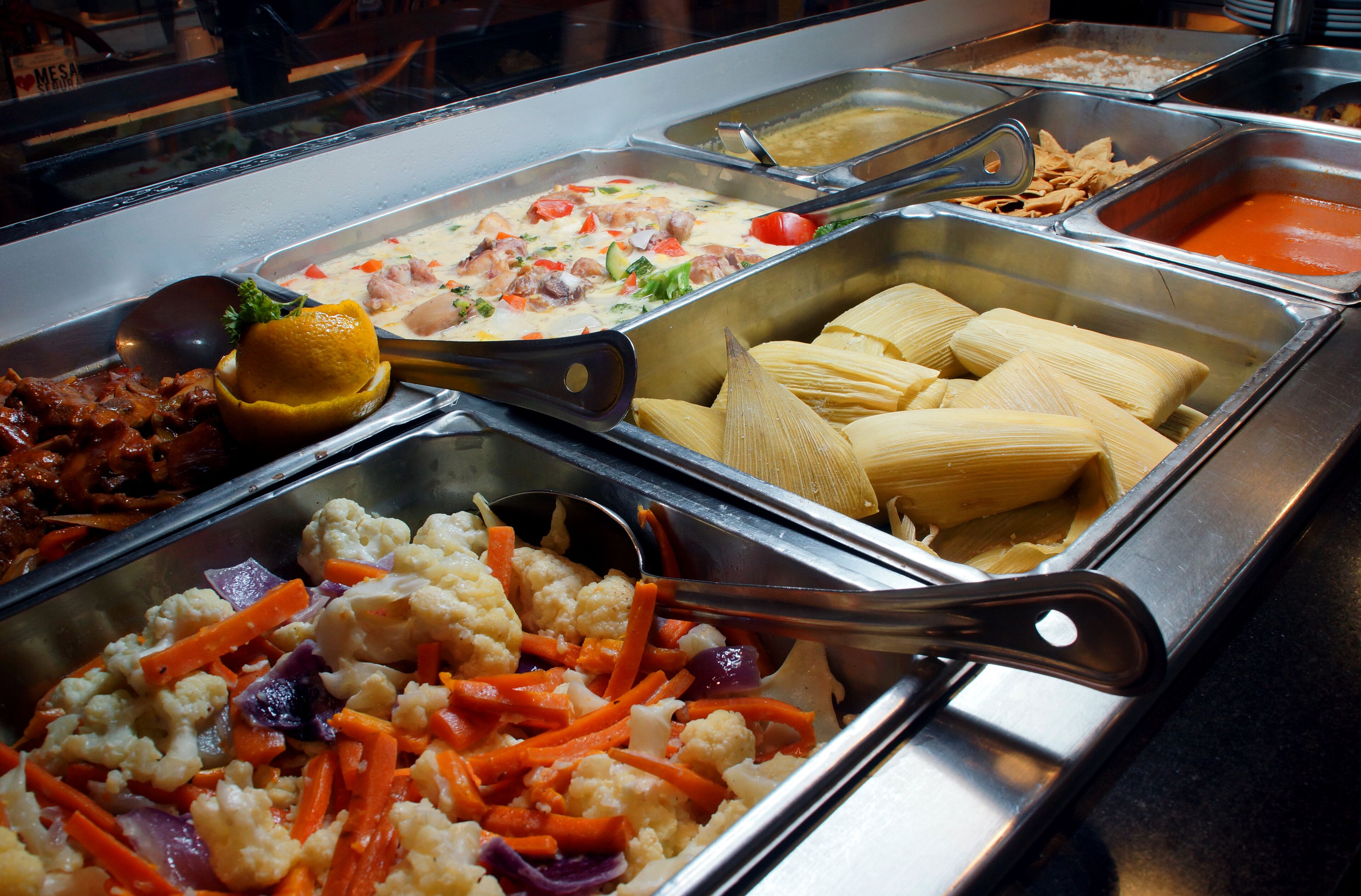 A buffet with various food options including vegetables, a salad, and tamales.