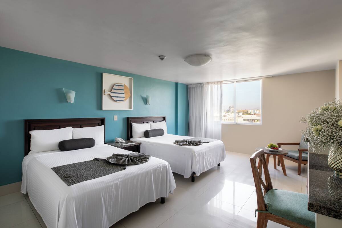 A hotel room with two beds, a dining area, and a view of the city.