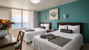 A hotel room with two beds, a large window with a view of the sea, a vase of flowers, and a framed fish artwork on the wall. - Don Pelayo Pacific Beach (Mazatlán)