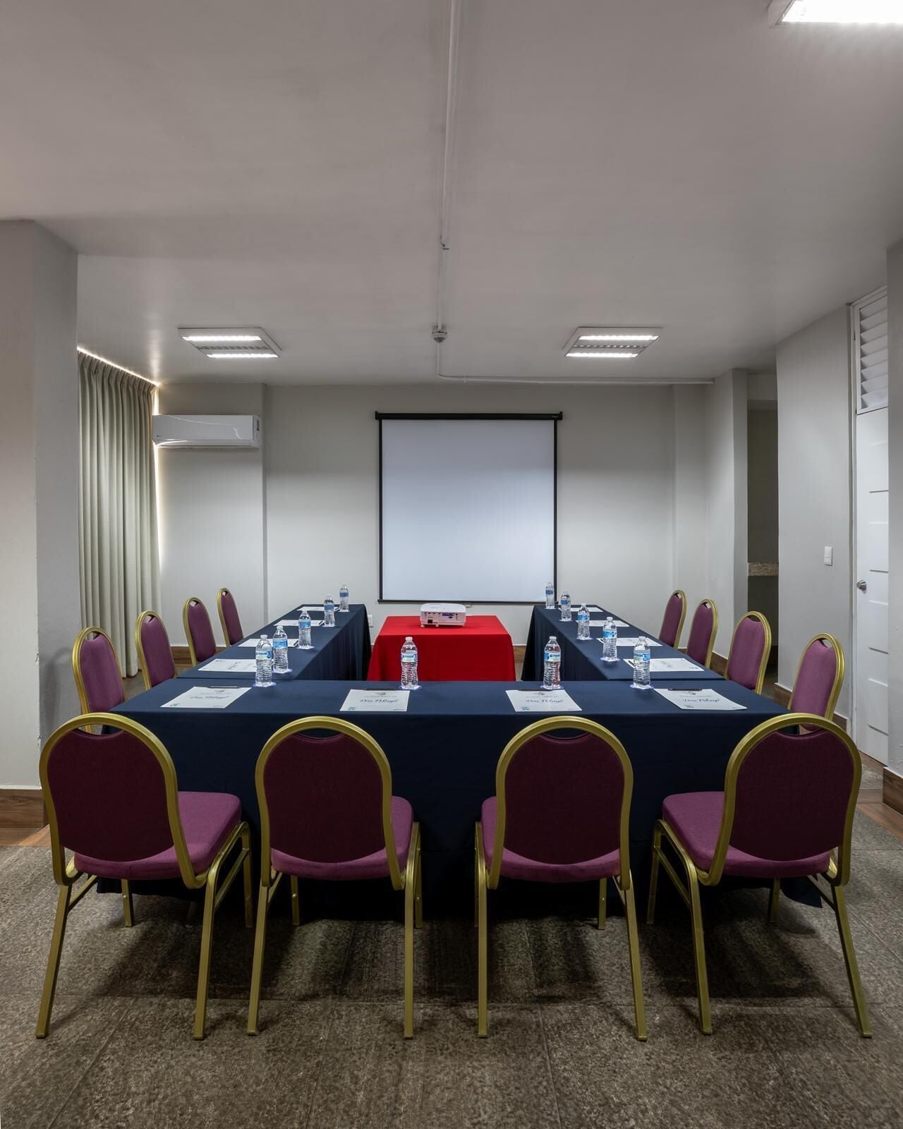 Une salle de conférence équipée d’une longue table, de chaises, d’un écran de projection et d’un appareil de climatisation.