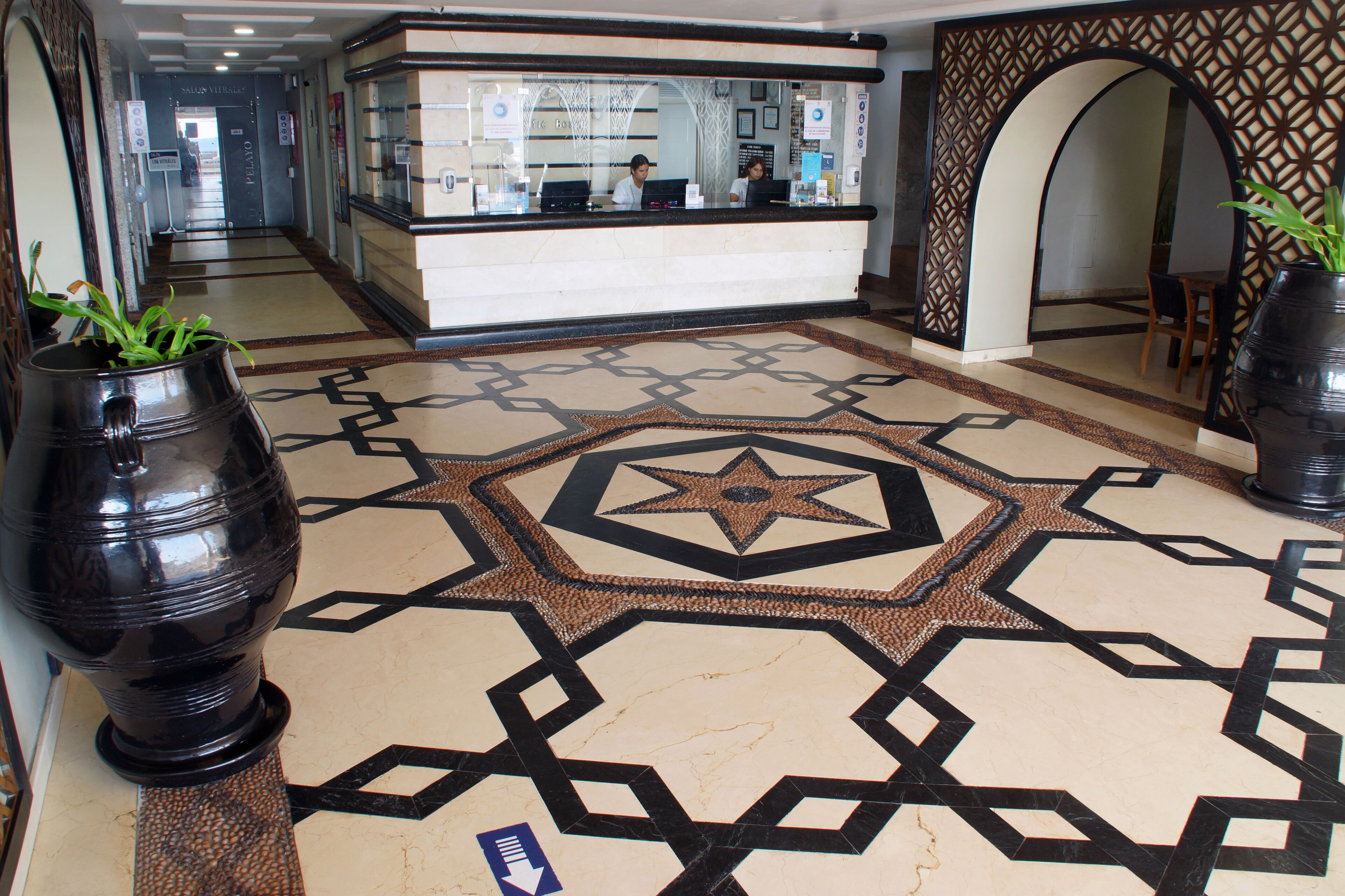 A reception area with a patterned floor, a reception desk, and two large potted plants.