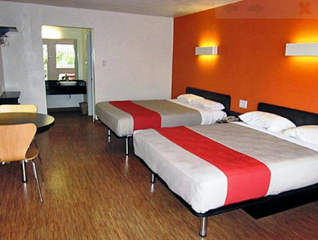 A hotel room with two beds, a desk, and a bathroom visible through an open door.