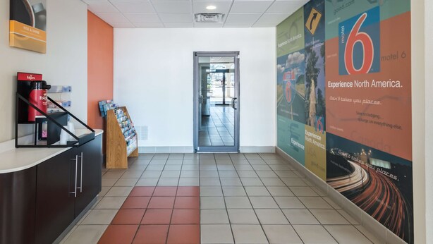 A hotel reception area with a coffee machine, a counter, and a poster advertising 'motel 6'. - Motel 6 Stephenville, TX (Stephenville)