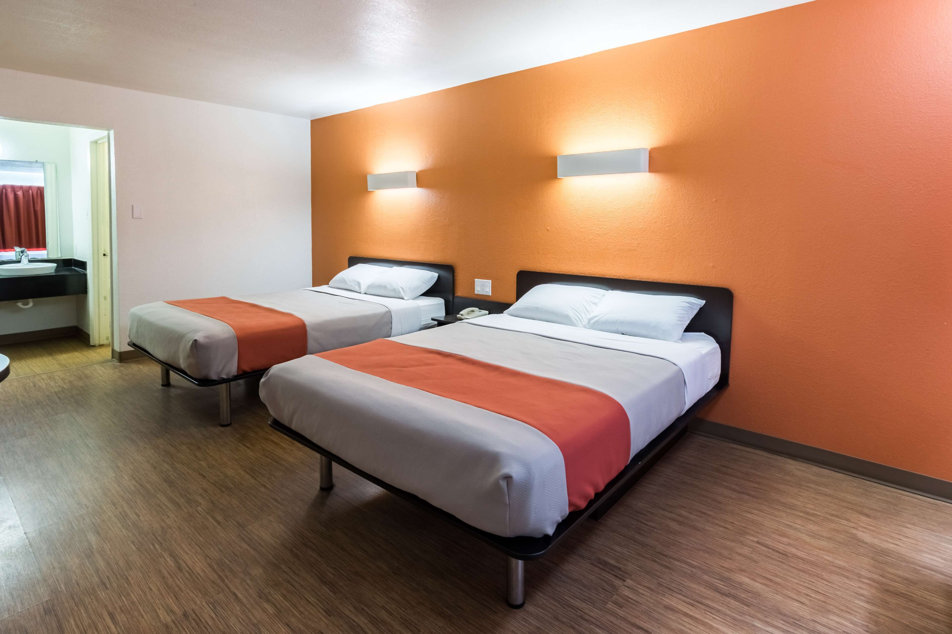 A hotel room with two beds, a bathroom, and a wooden floor.