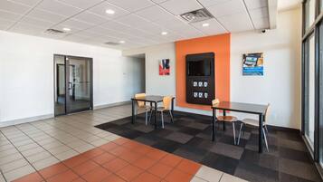 A modern office space with a meeting room, two tables with chairs, a large window, and a wall-mounted screen.