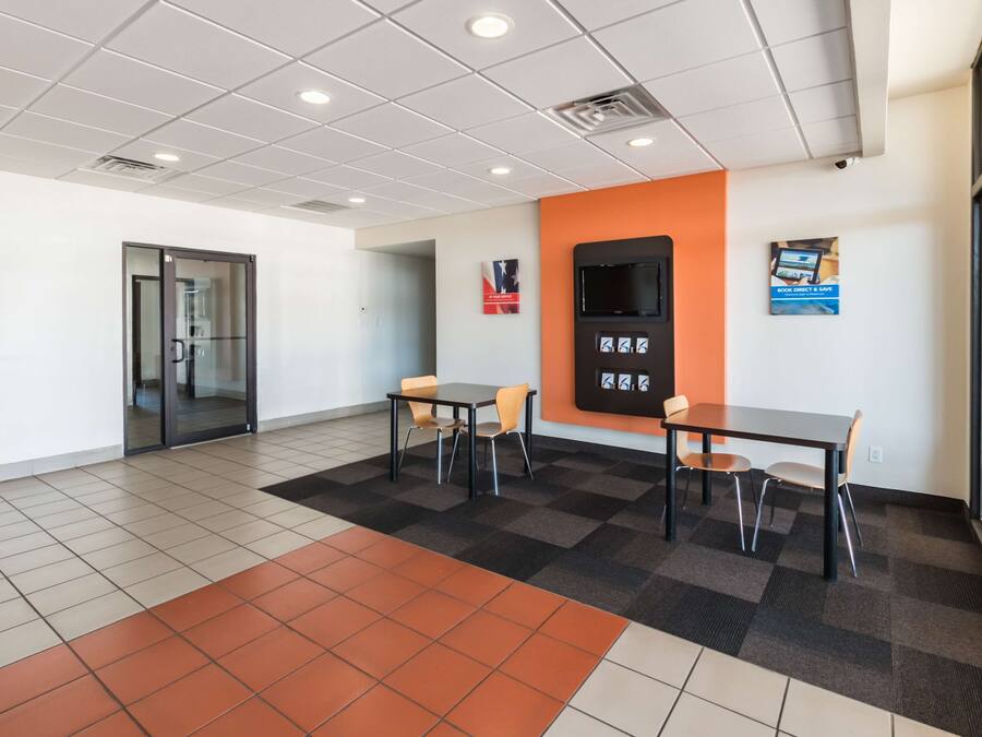A modern office space with a meeting room, two tables with chairs, a large window, and a wall-mounted screen.