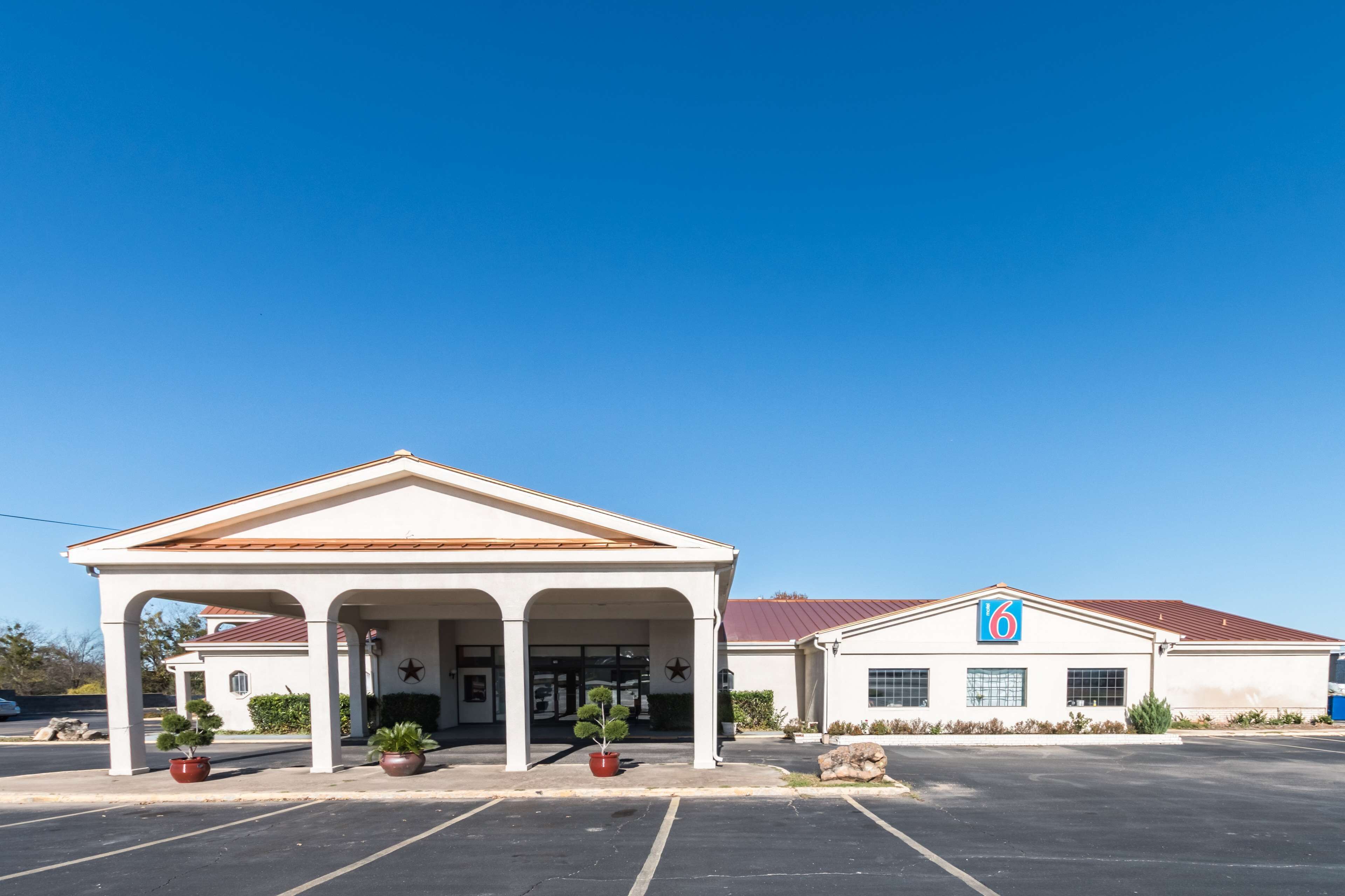 A hotel with a covered entrance, a parking lot, and a building with a '6' sign.