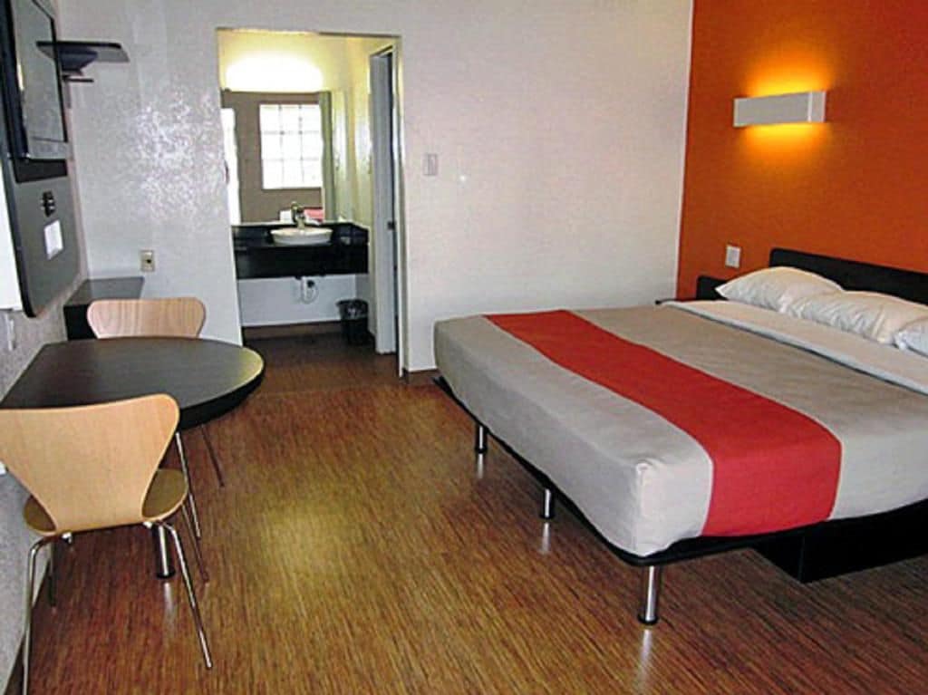 A hotel room with a bed, a desk, a chair, a mirror, and a bathroom.