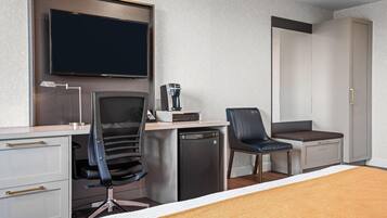 A hotel room with a bed, a desk with a chair, a coffee machine, a TV, and a wardrobe.