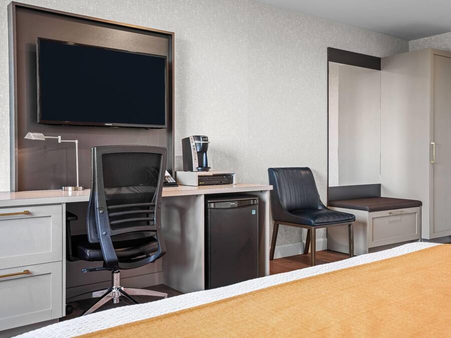 Une chambre d’hôtel comprenant un lit, un bureau avec une chaise, une machine à café, une télévision et une armoire.