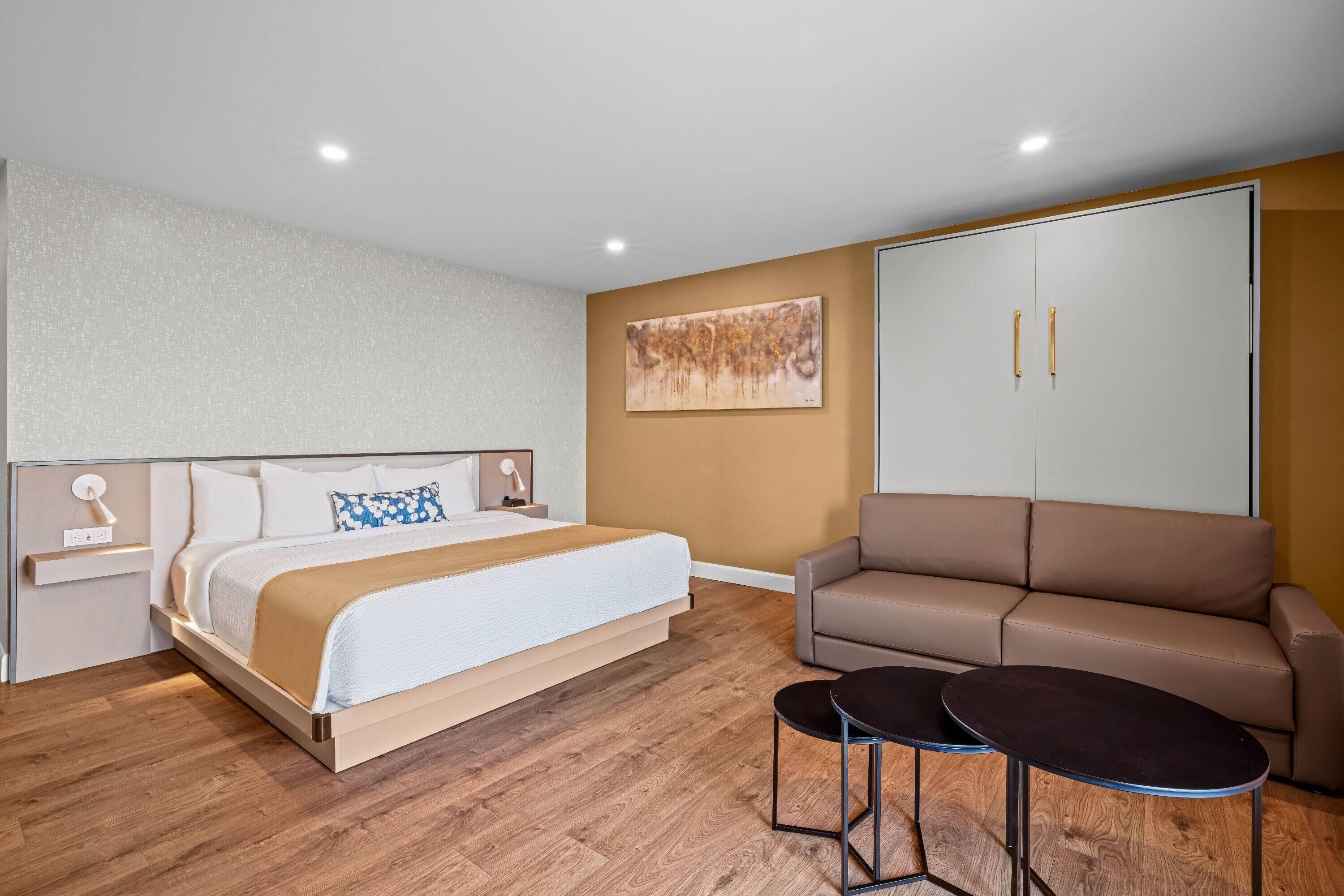 Una habitación de hotel moderna con una cama, un sofá y dos mesitas.