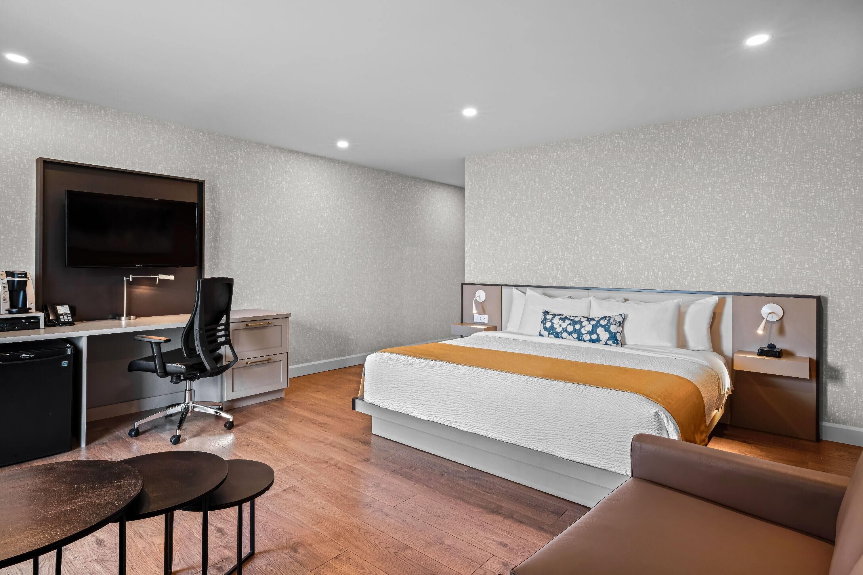 A modern hotel room with a large bed, a desk with a computer, a chair, and a TV mounted on the wall.