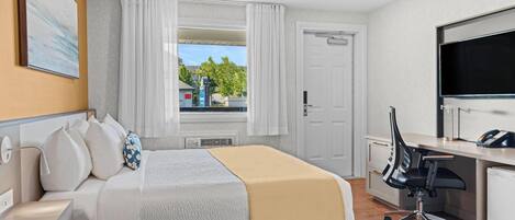 Habitación de hotel con cama, escritorio, silla, televisor y ventana con cortinas.