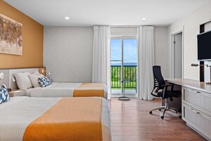 Habitación de hotel con dos camas, un escritorio, una silla, un televisor y un balcón con vistas.