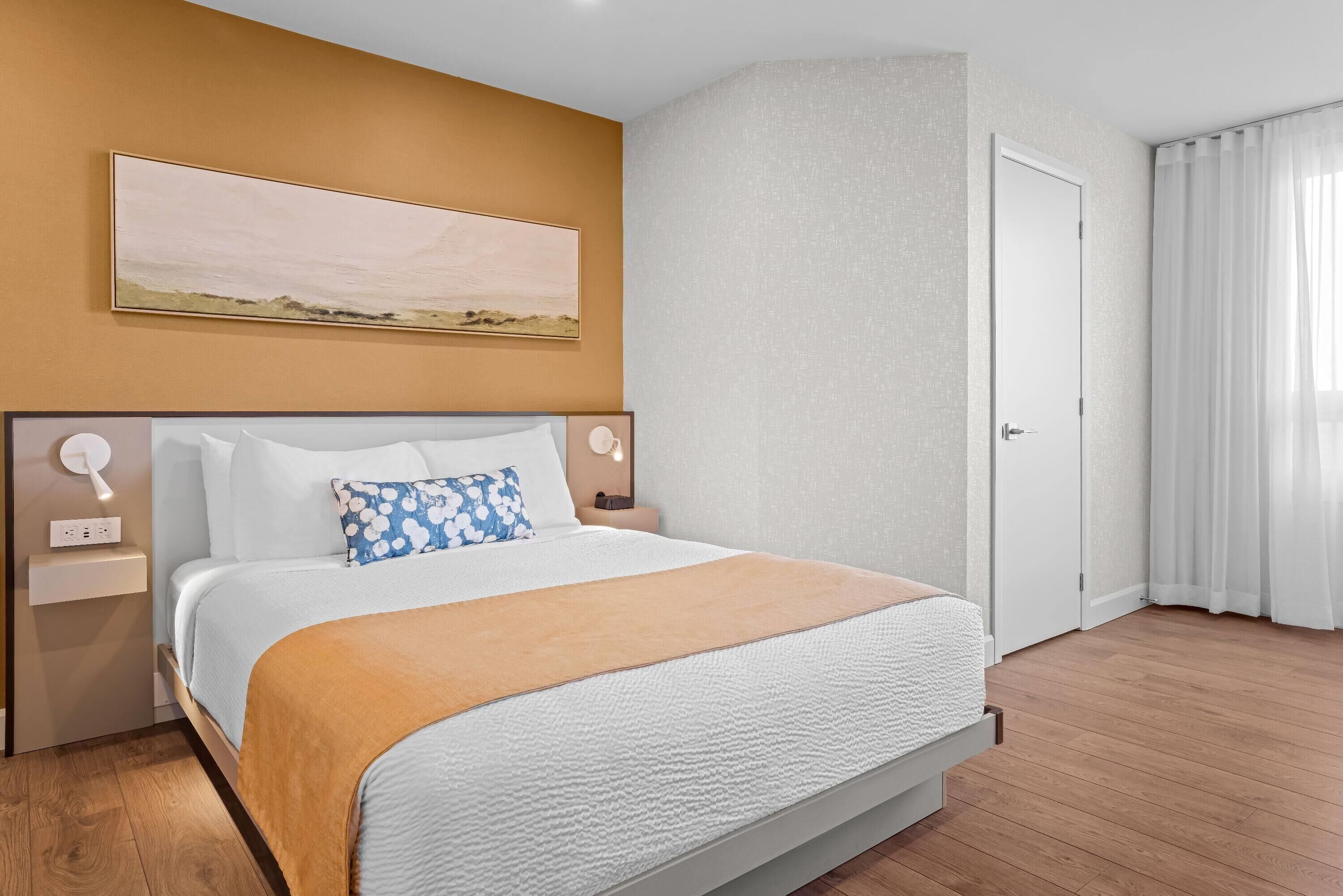 Una habitación de hotel con una cama grande, un cuadro en la pared, una puerta y una ventana con cortinas.