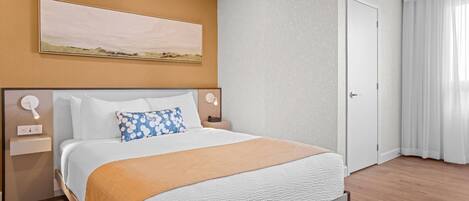 Una habitación de hotel con una cama grande, un cuadro en la pared, una puerta y una ventana con cortinas.