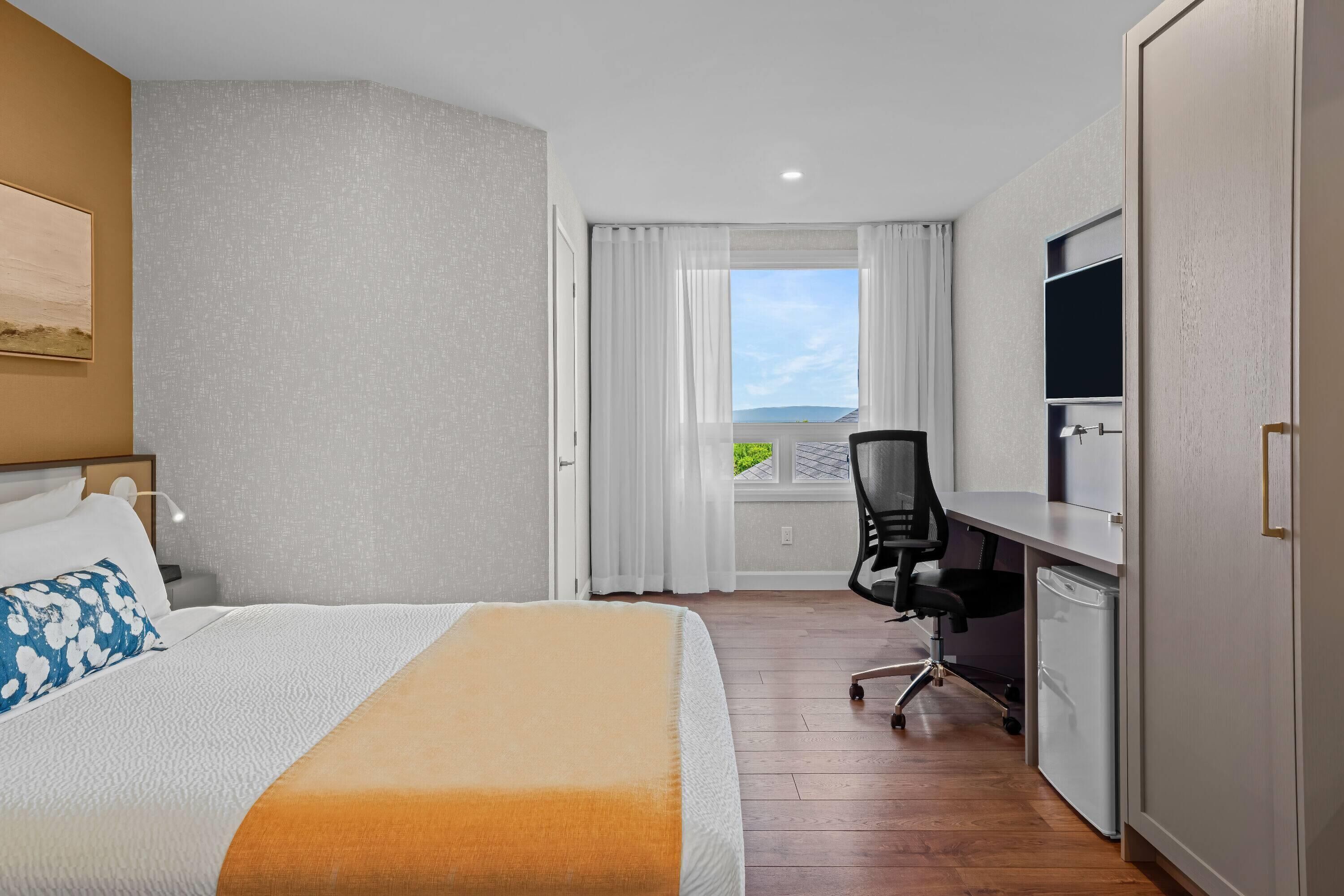 A hotel room with a bed, a desk, a chair, a television, and a window with a view.