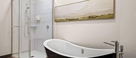 Un baño moderno con ducha de vidrio, bañera independiente y un cuadro colgado.