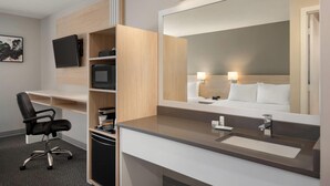 Una habitación de hotel moderna con escritorio, silla, televisor y un espejo grande.