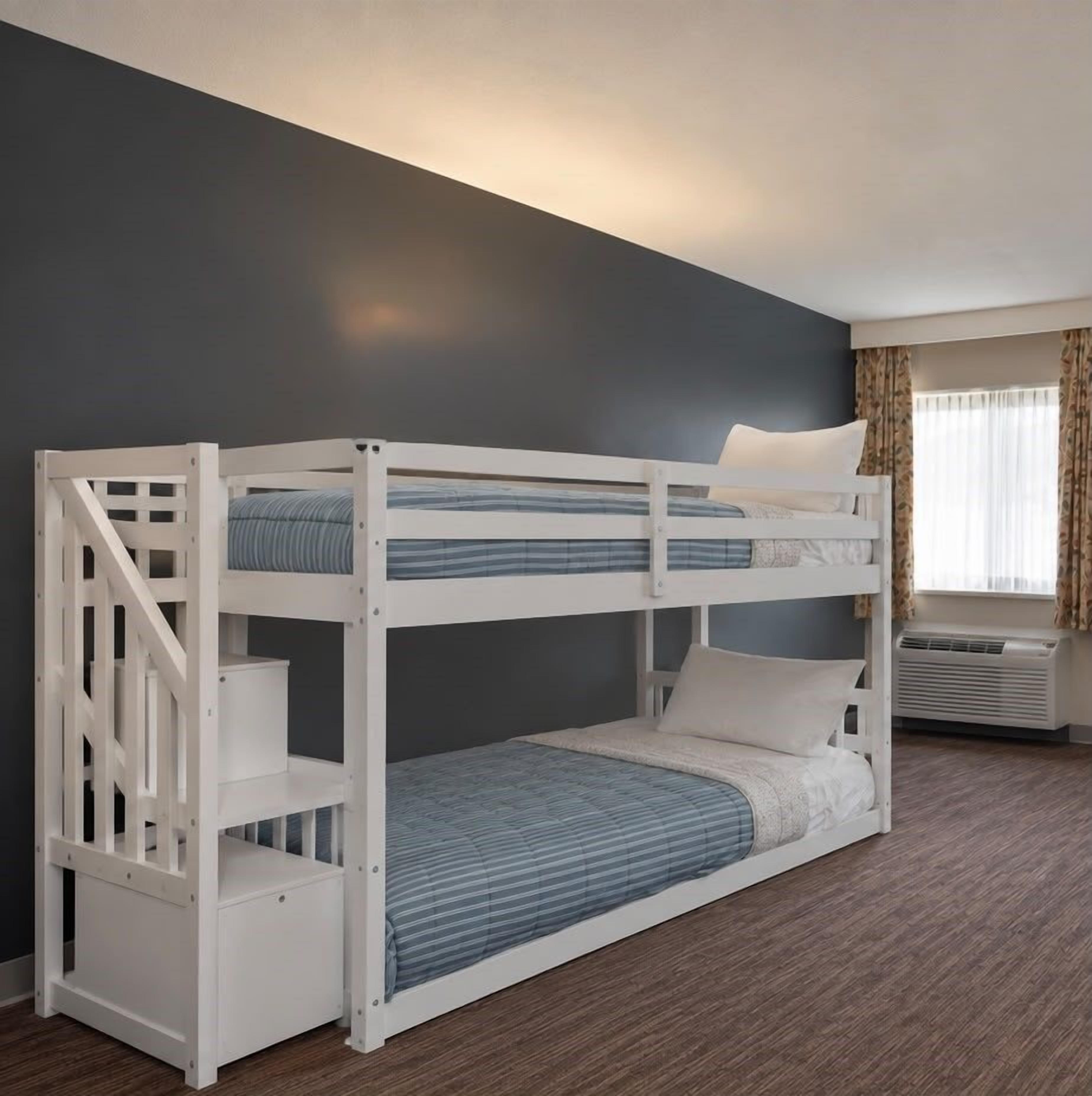 A bunk bed with a ladder, a window with curtains, and an air conditioning unit.