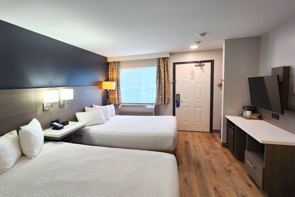 A hotel room with two beds, a desk, a TV, and a window with curtains.